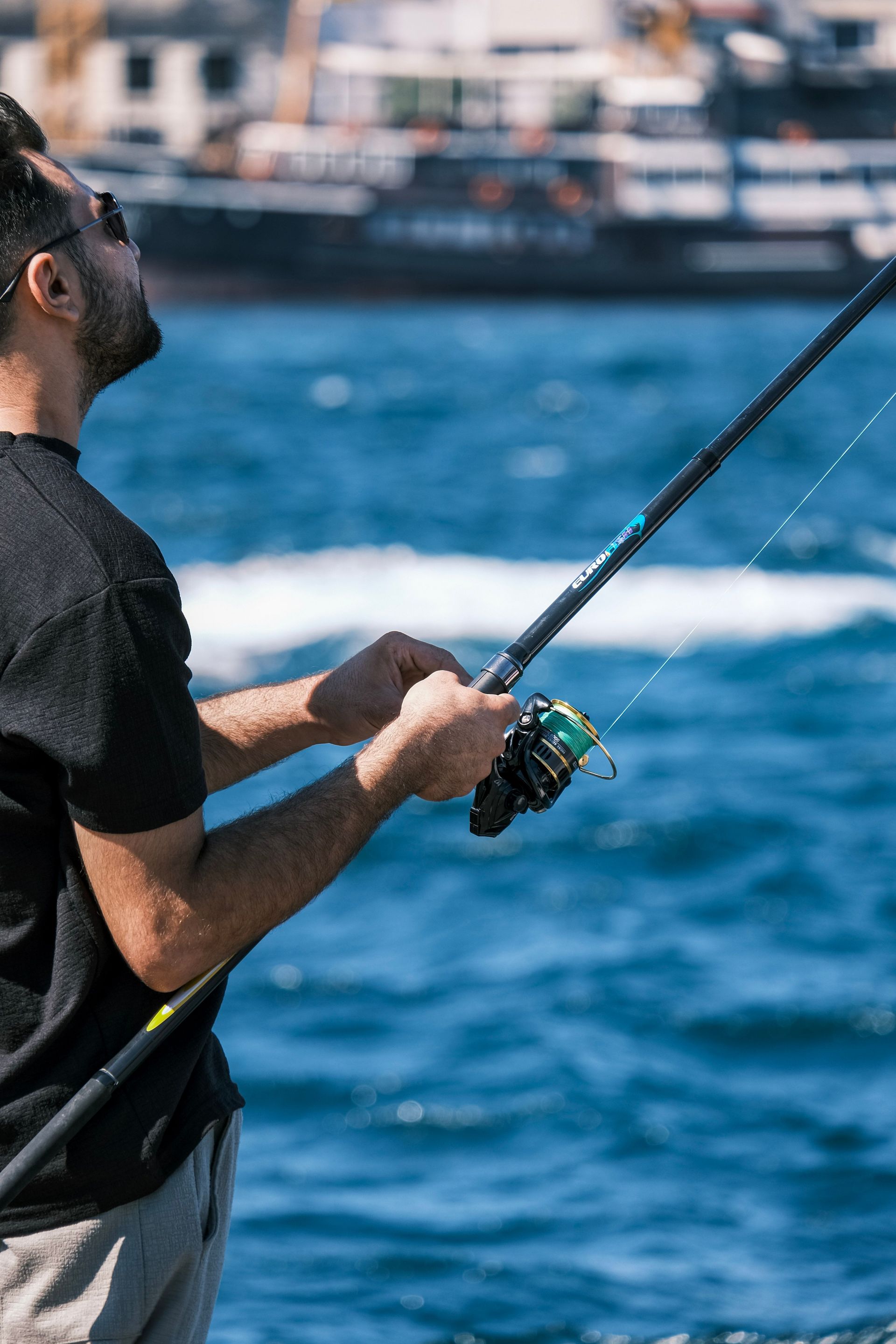Focused man fishing with rod in scenic waterfront setting on a sunny day.